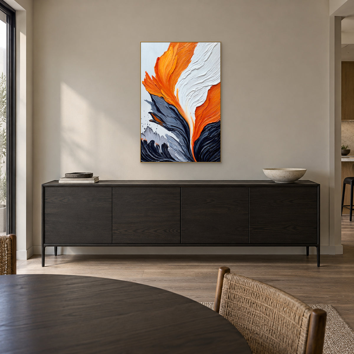 Tableau texturé orange et blanc dans un cadre champagne, au-dessus d’un buffet foncé dans une salle à manger