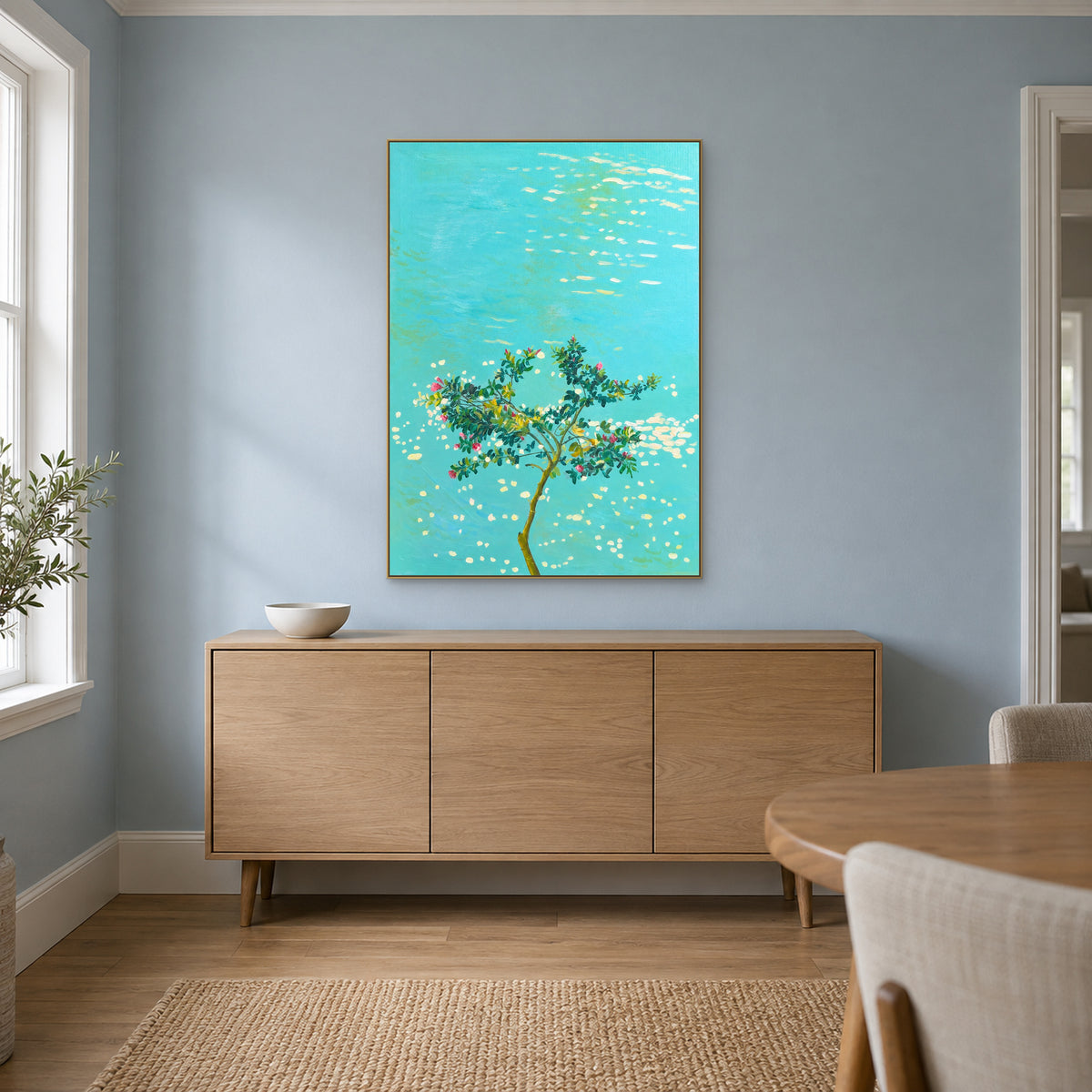 Fleurs sur l’eau turquoise dans un cadre champagne au-dessus d’un buffet ton chêne, sur un mur bleu poudré de salle à manger