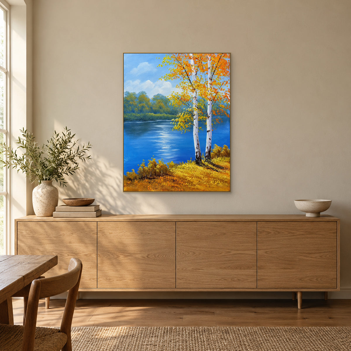 Birches beside a blue river in a champagne-coloured frame above a wooden sideboard