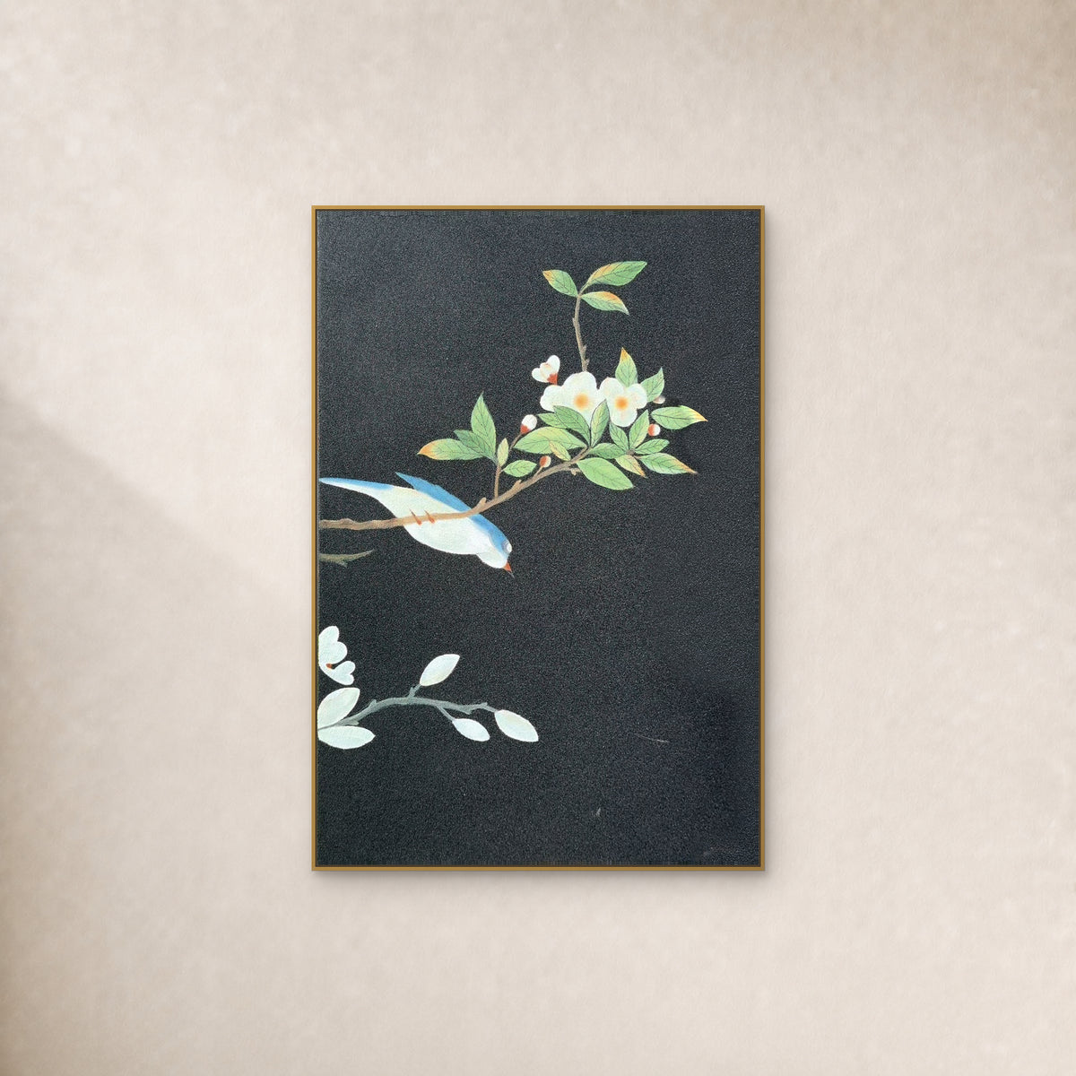 Blue-and-ivory bird and white blossoms on charcoal in a slim gold-tone frame against an ivory wall