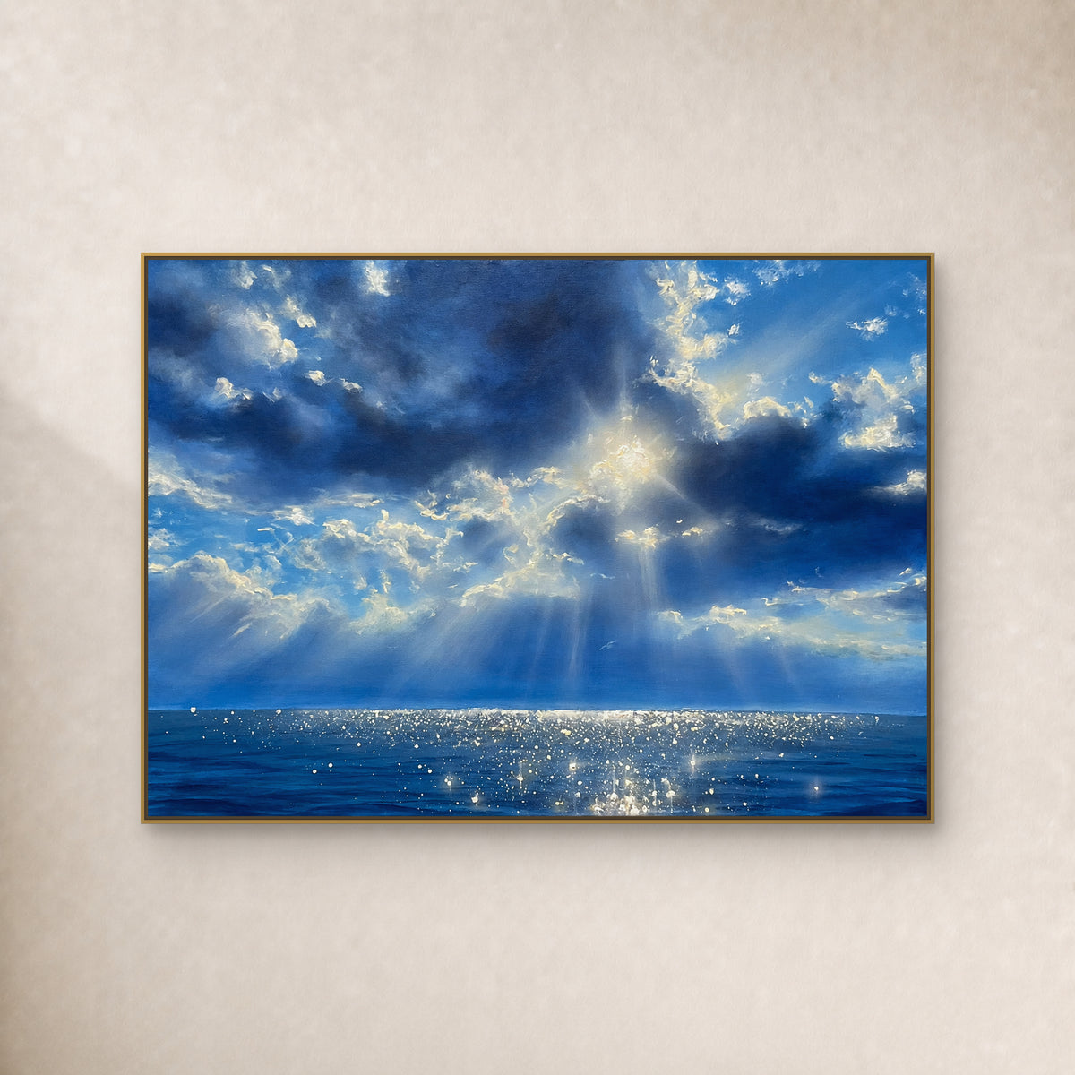 Blue cloud seascape with sunrays and silver-white sea reflections in a thin gold floating frame on an ivory wall.