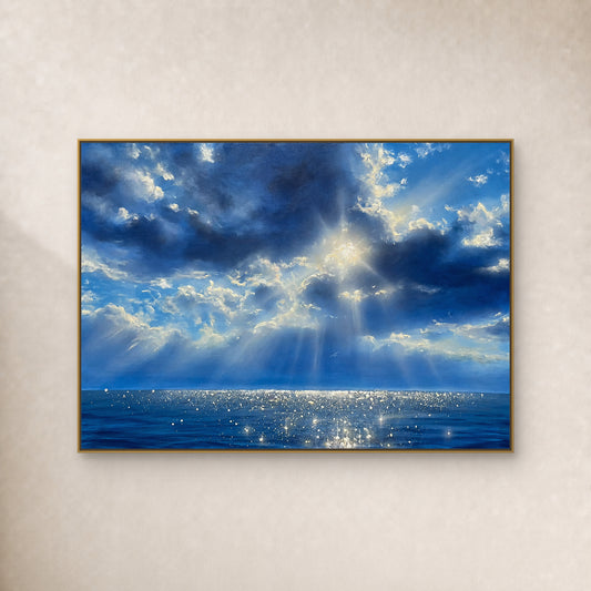 Blue cloud seascape with sunrays and silver-white sea reflections in a thin gold floating frame on an ivory wall.