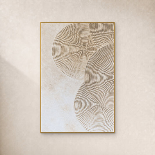 Cercles concentriques couleur sable sur un fond ivoire texturé, dans un fin cadre doré sur un mur ivoire uni.