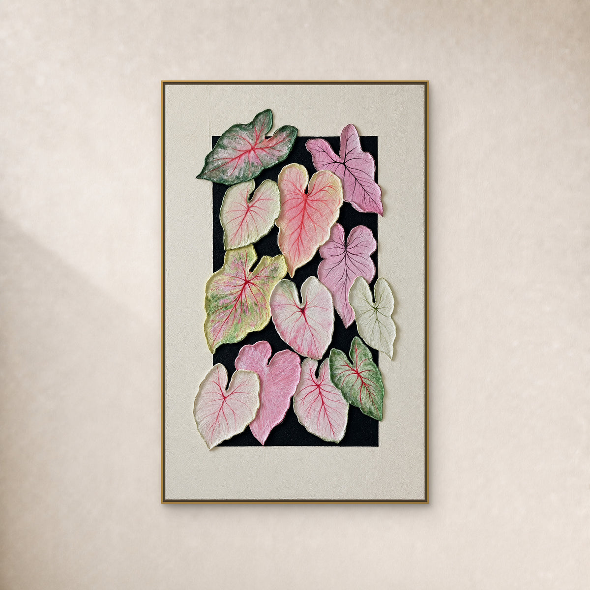 Douze feuilles de caladium roses, lilas et vertes sur fond peint noir entouré d’ivoire, dans un fin cadre flottant doré sur un mur ivoire