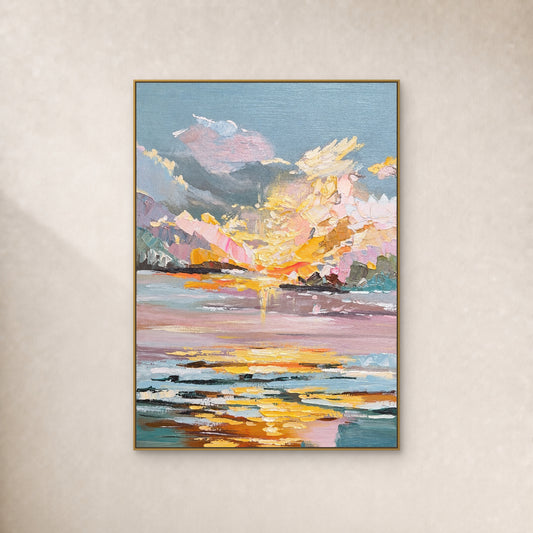 Pink and cream sunset clouds above mauve water with golden reflections, in a thin gold-tone frame on an ivory wall