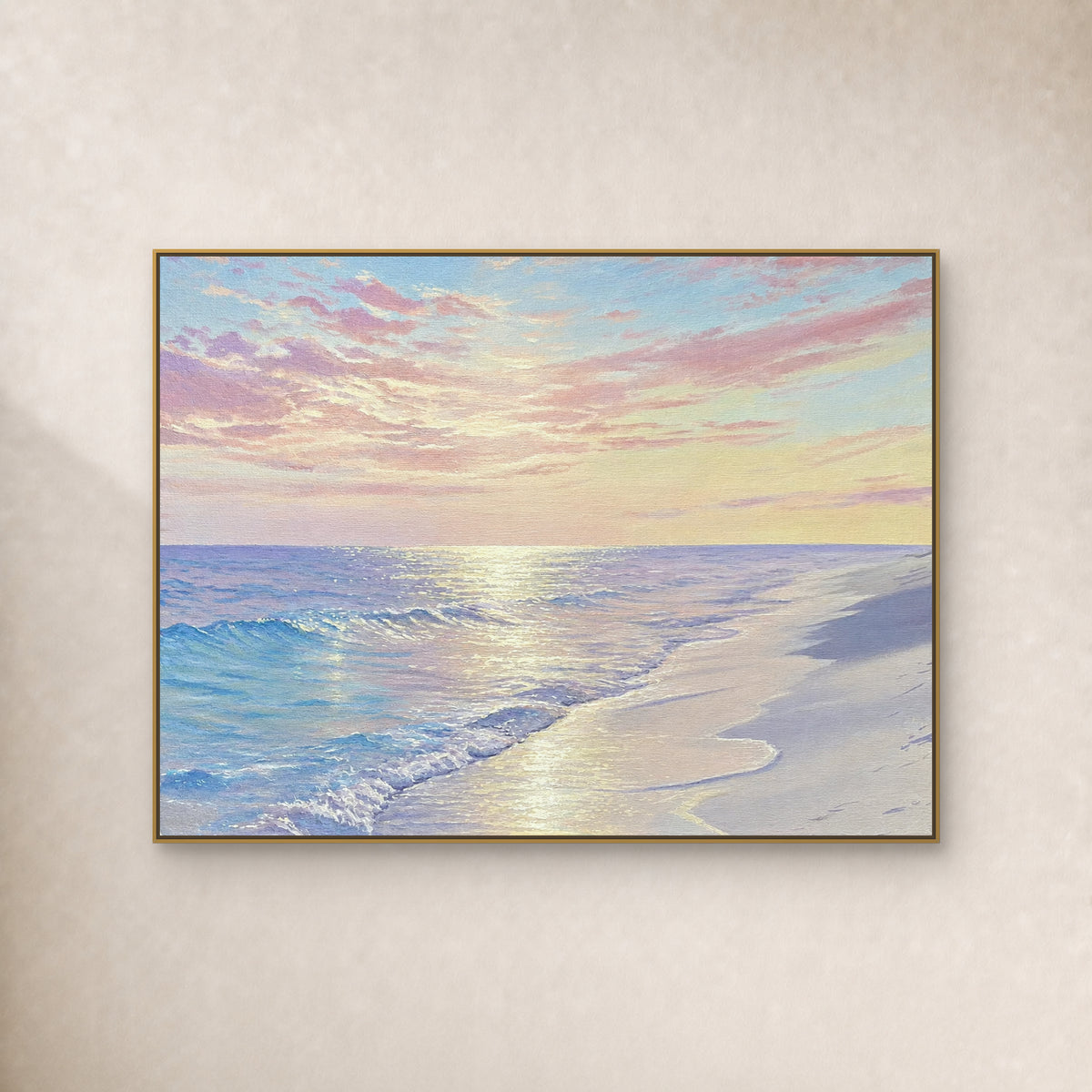 Pastel beach painting with pink clouds, blue surf and reflected light in a slim gold-tone frame on an ivory wall