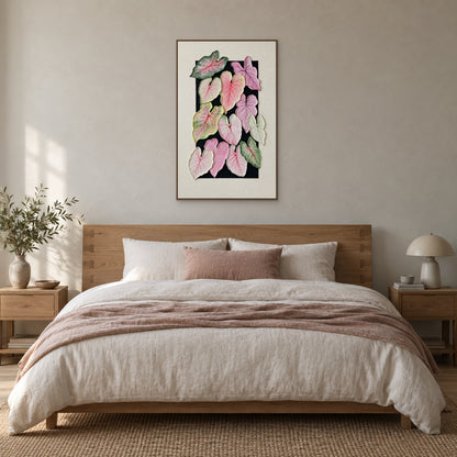Tableau vertical de caladium dans un cadre flottant ton bois, centré au-dessus d’un lit en chêne aux draps ivoire et rose poudré