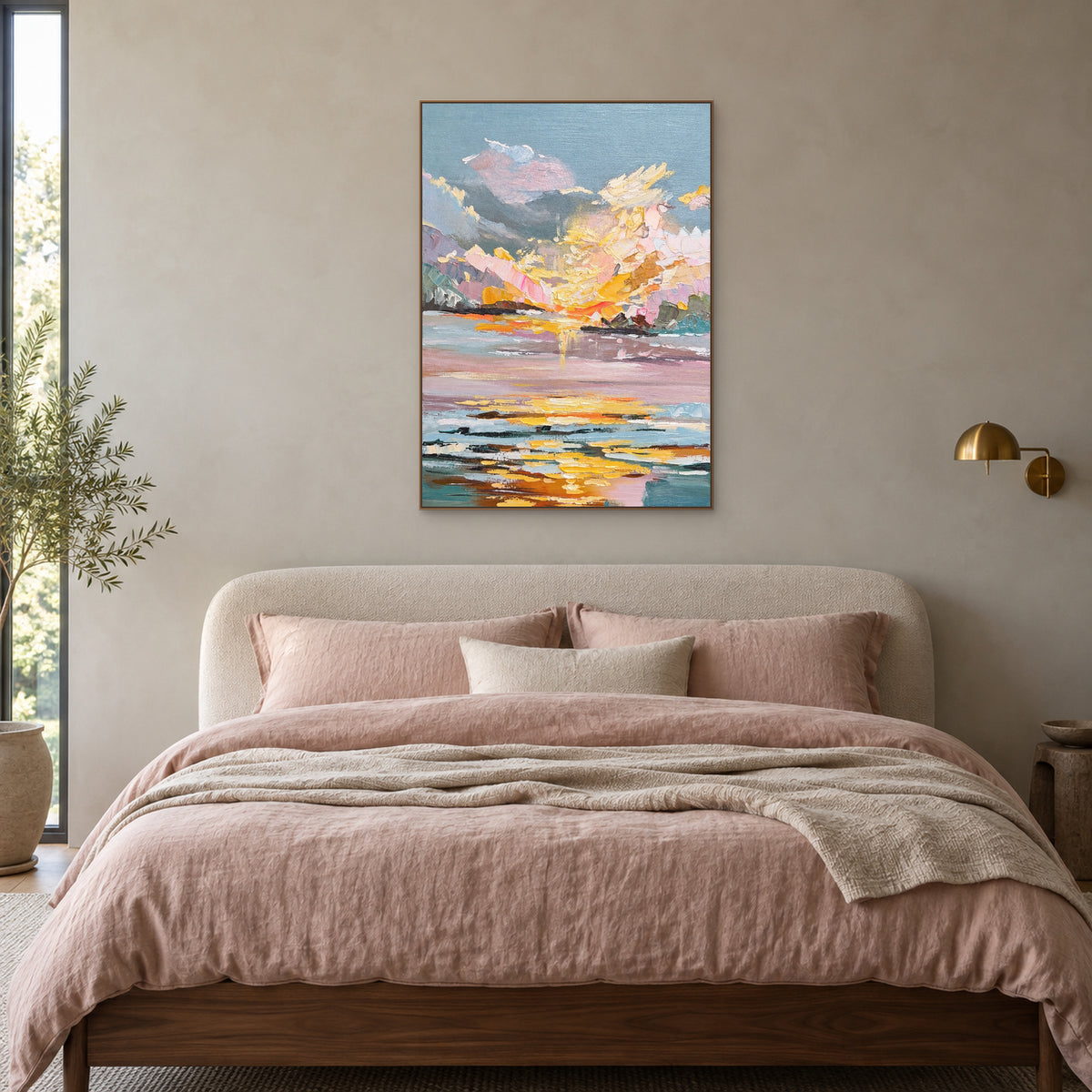 Vertical pink sunset painting in an oak-tone frame above a bed with blush linen