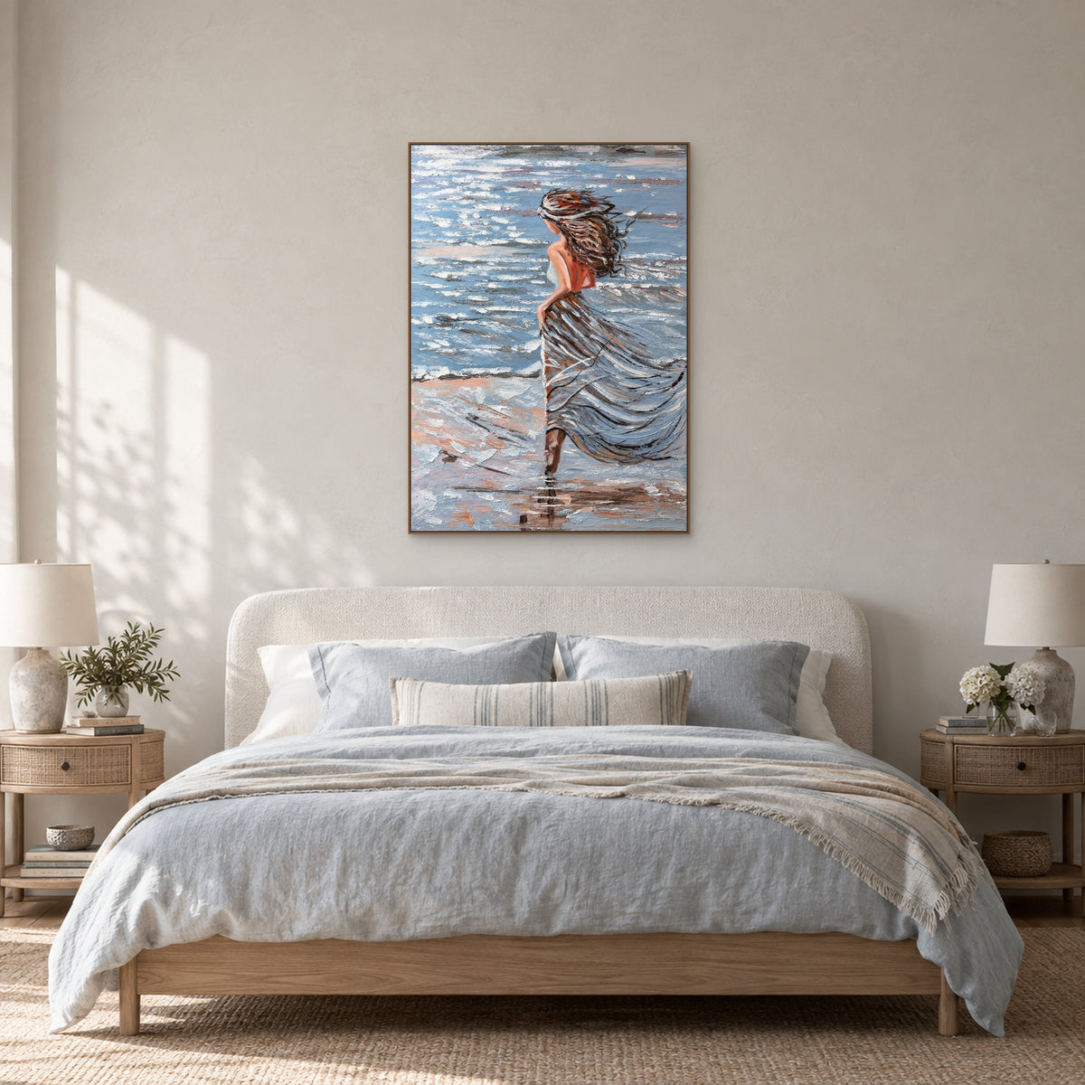 Tableau de femme au bord de mer dans un cadre flottant ton chêne, centré au-dessus d'une tête de lit ivoire arrondie et de linge bleu pâle