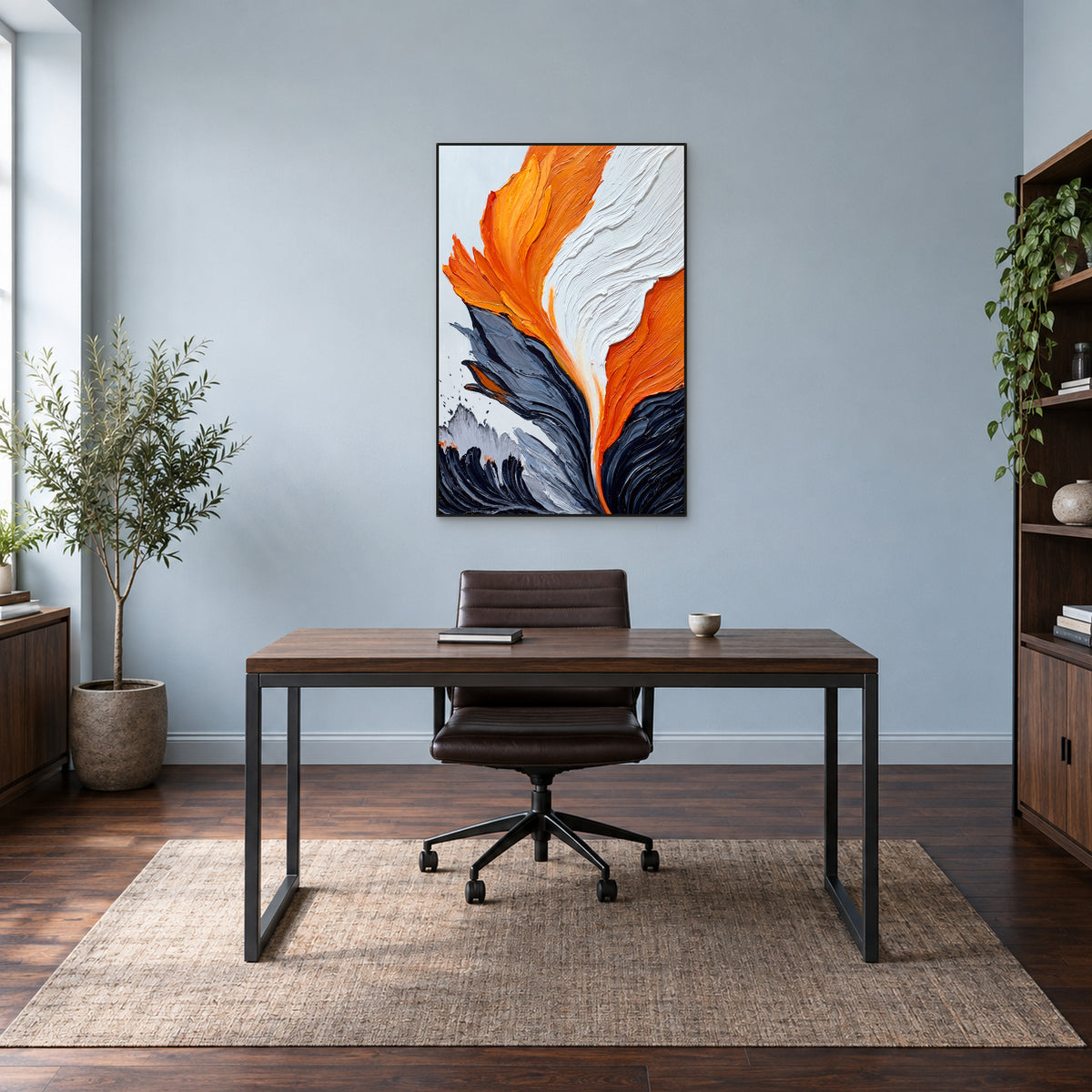 Tableau abstrait orange et noir charbon dans un fin cadre noir, au-dessus d’un bureau en bois contre un mur bleu-gris