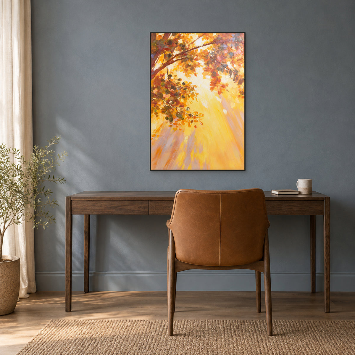 Golden autumn tree painting in a thin black floating frame above a dark wood desk against a blue-grey wall.