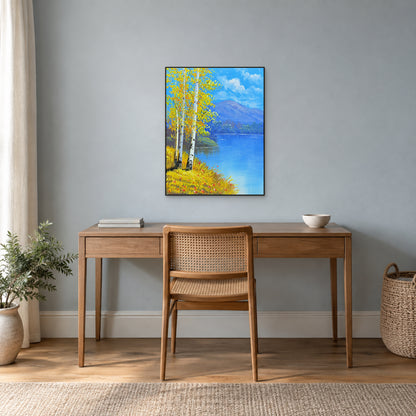Autumn birches and an open blue lake in a thin black frame above a wooden writing desk.