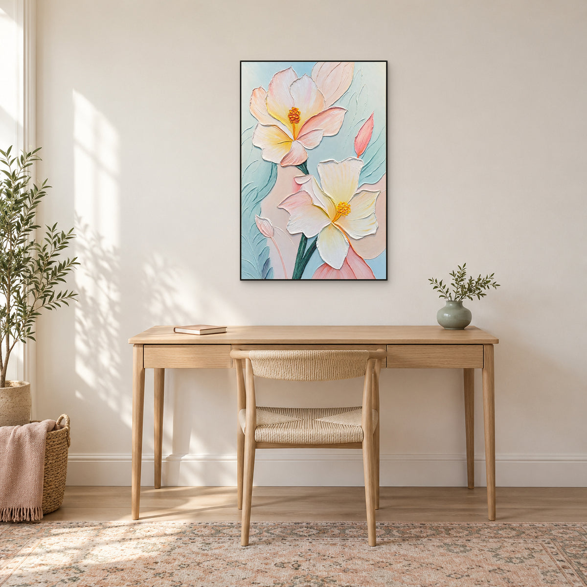Tableau floral pastel vertical dans un fin cadre noir au-dessus d’un bureau en bois clair et d’une chaise tressée