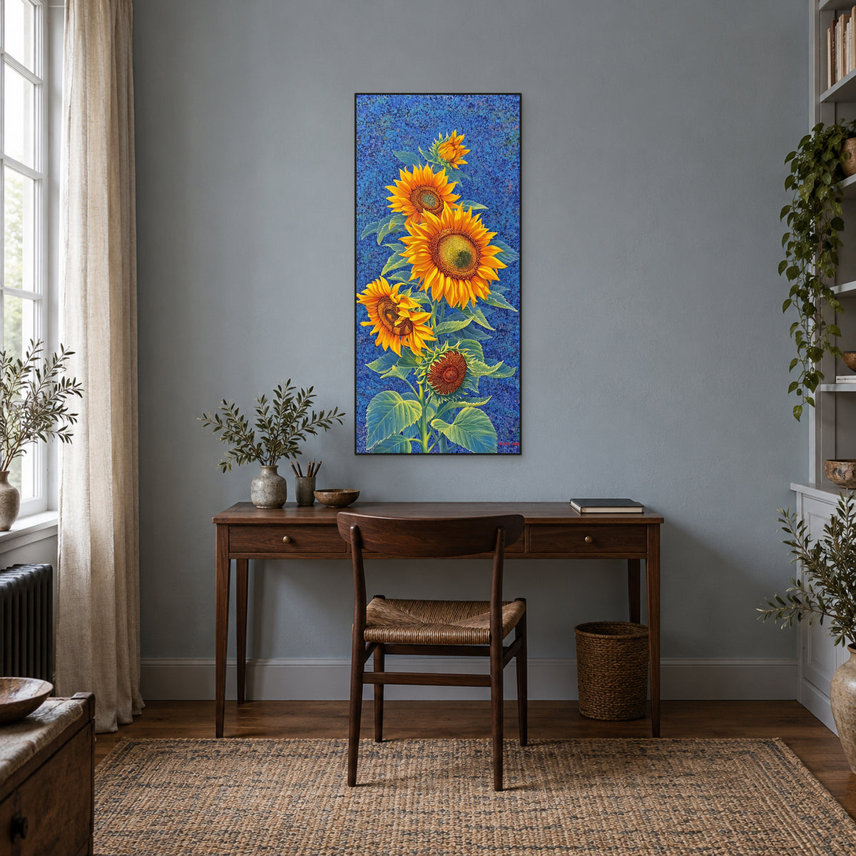 Blue and yellow sunflower painting in a black frame above a dark wooden desk on a blue-grey wall