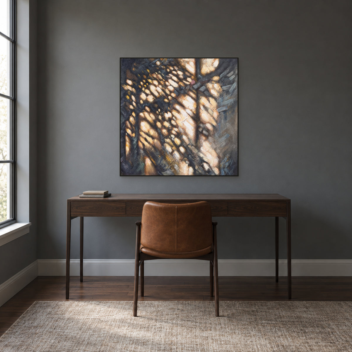 Ochre and charcoal square painting in a black floating frame above a desk against a dark wall
