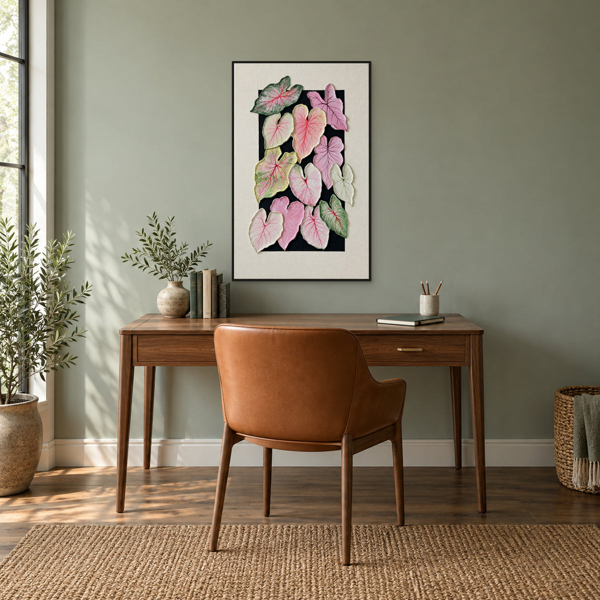 Tableau de caladium rose et vert dans un cadre flottant noir, au-dessus d’un bureau en noyer contre un mur vert doux