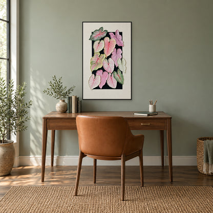 Tableau de caladium rose et vert dans un cadre flottant noir, au-dessus d’un bureau en noyer contre un mur vert doux