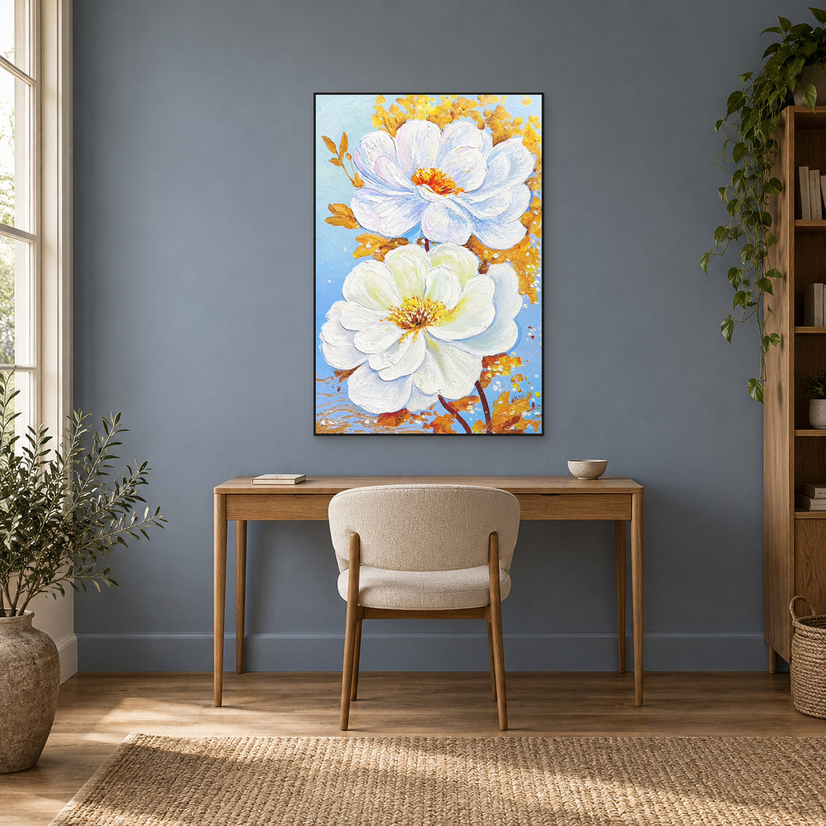 White floral painting in a thin black floating frame above a wooden desk against a muted blue wall.