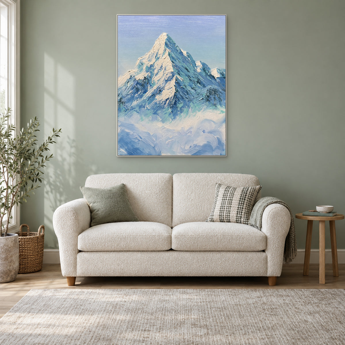 Tableau vertical de montagne enneigée dans un cadre blanc, au-dessus d’un petit canapé crème sur un mur sauge.