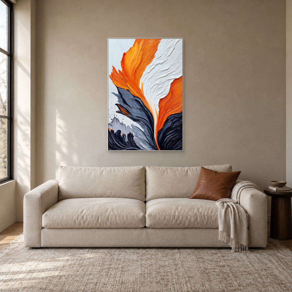 Tableau abstrait texturé orange et blanc dans un fin cadre blanc, au-dessus d’un canapé crème dans un coin lecture
