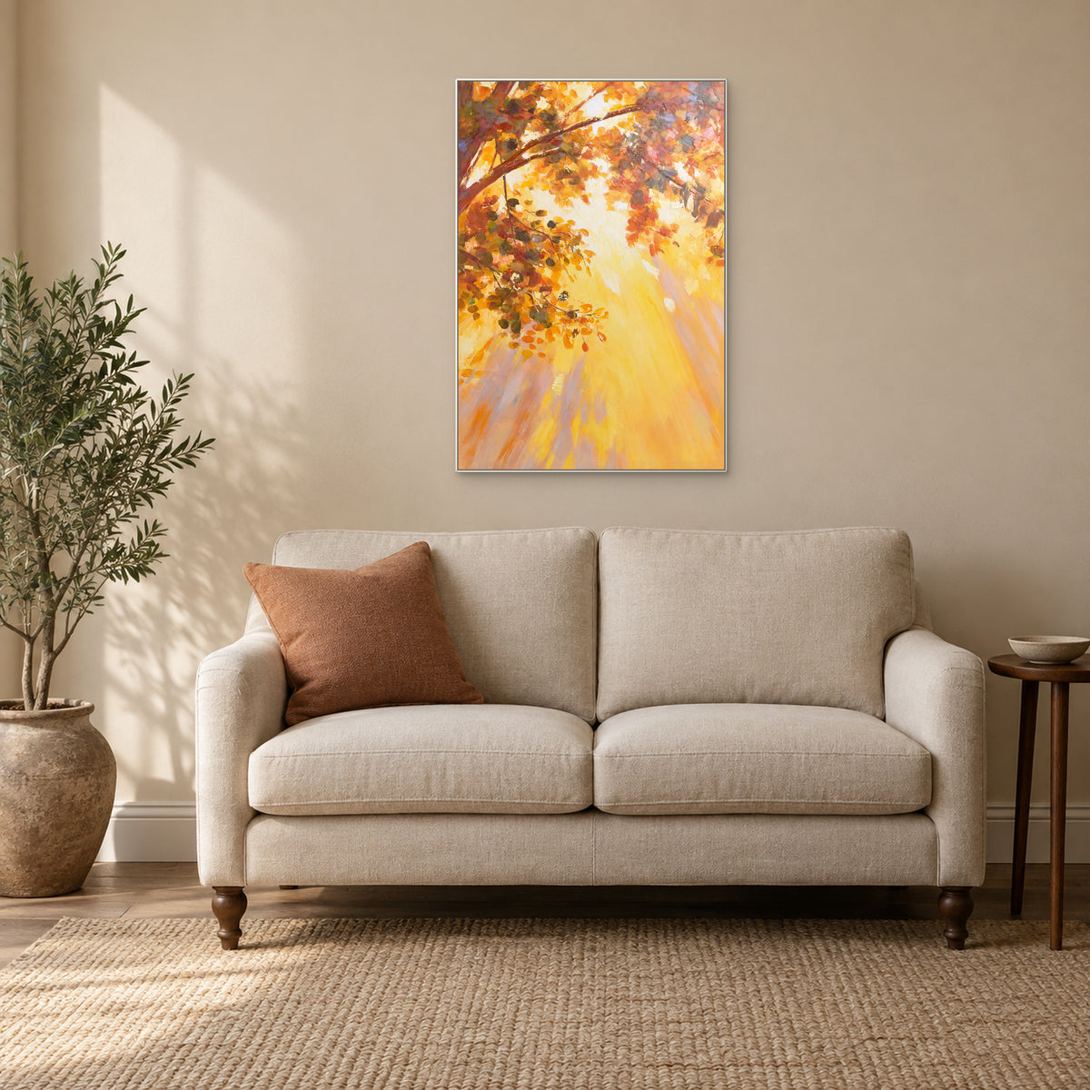 Autumn foliage painting with a slim white frame above a cream loveseat and terracotta cushion.