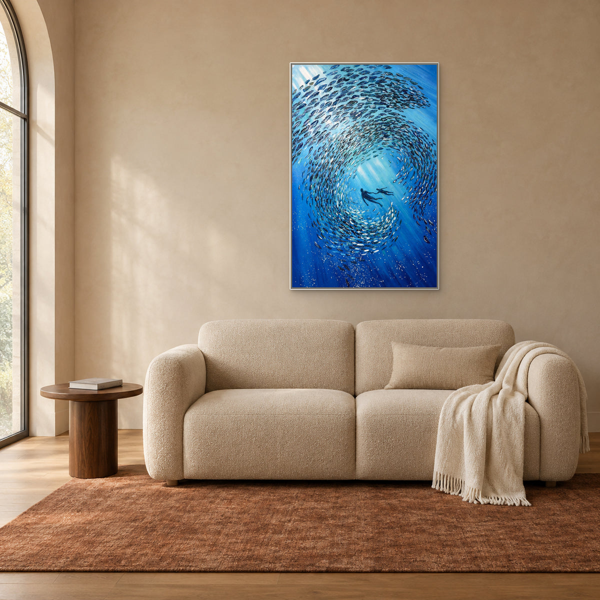 Tableau vertical de poissons bleus dans un cadre flottant blanc, au-dessus d’un canapé couleur biscuit près d’une fenêtre cintrée