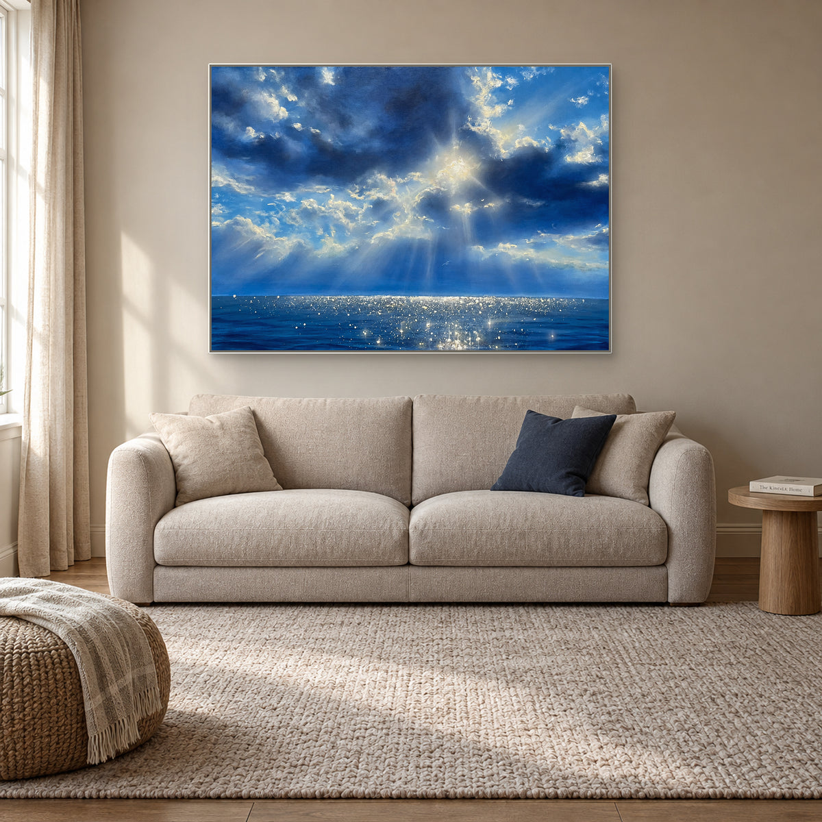 Blue cloud and sunbeam painting in a white floating frame above a beige settee in a reading nook.