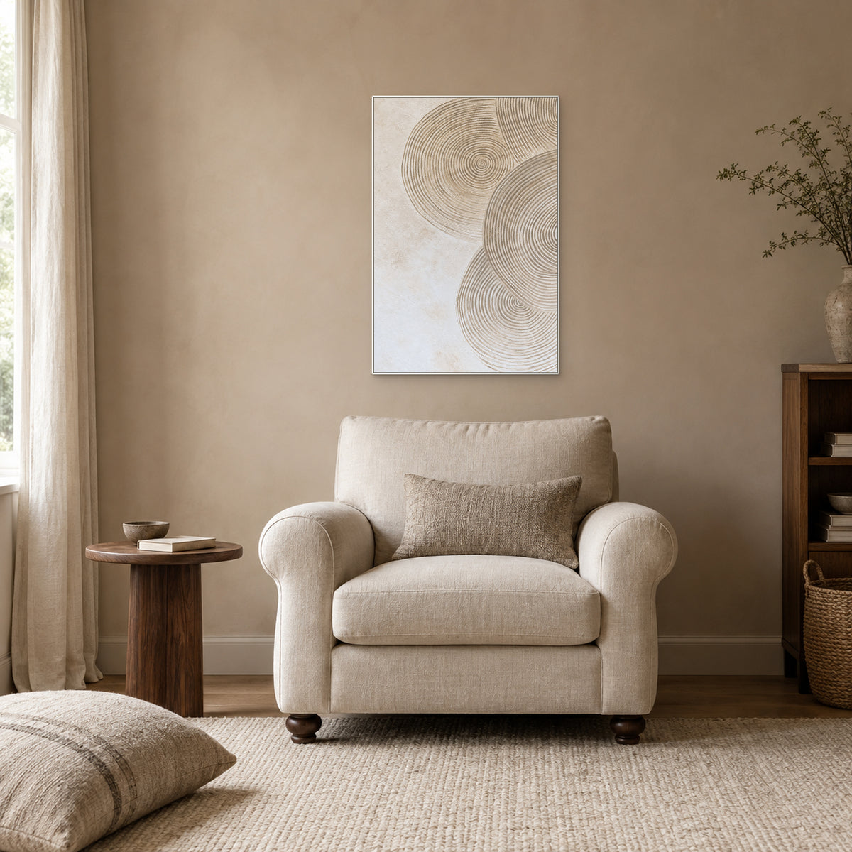Neutral circular relief in a white frame above an ivory armchair, beside a low wooden reading table.