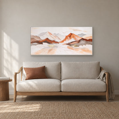 Textured mountain panorama in a white floating frame above an ivory reading sofa with a terracotta cushion