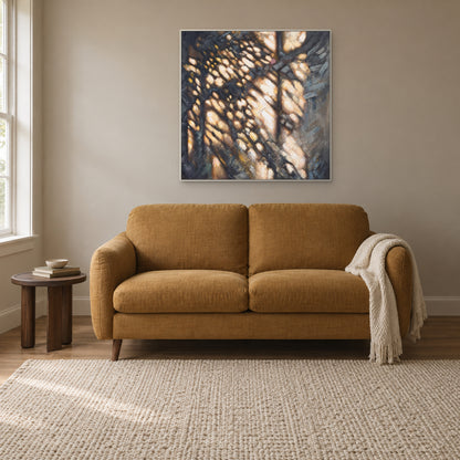 Textured light-and-shadow abstract in a white floating frame above an ochre reading sofa