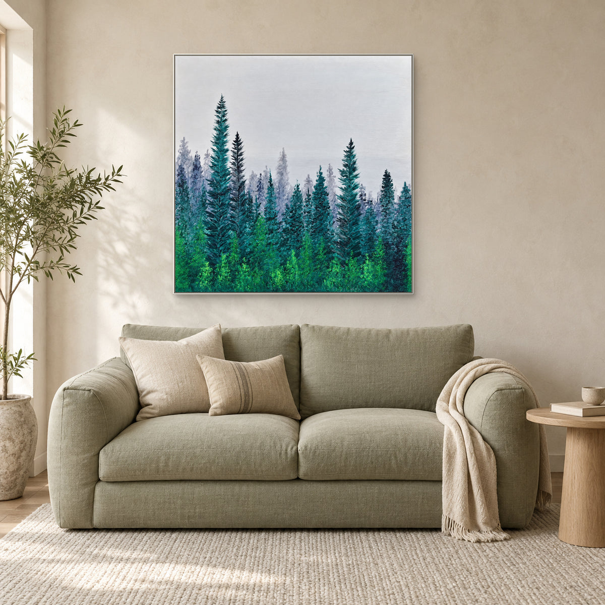 White-framed misty pine painting above a sage-green loveseat beside a small wooden table