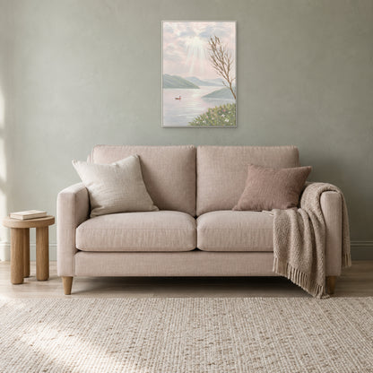 Paysage pastel dans un cadre flottant blanc au-dessus d'un petit canapé rose en lin