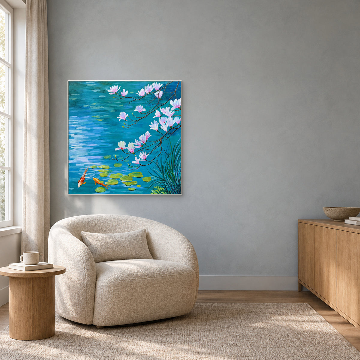 Pink magnolias and two koi on blue water, displayed in a white frame above a rounded cream reading chair