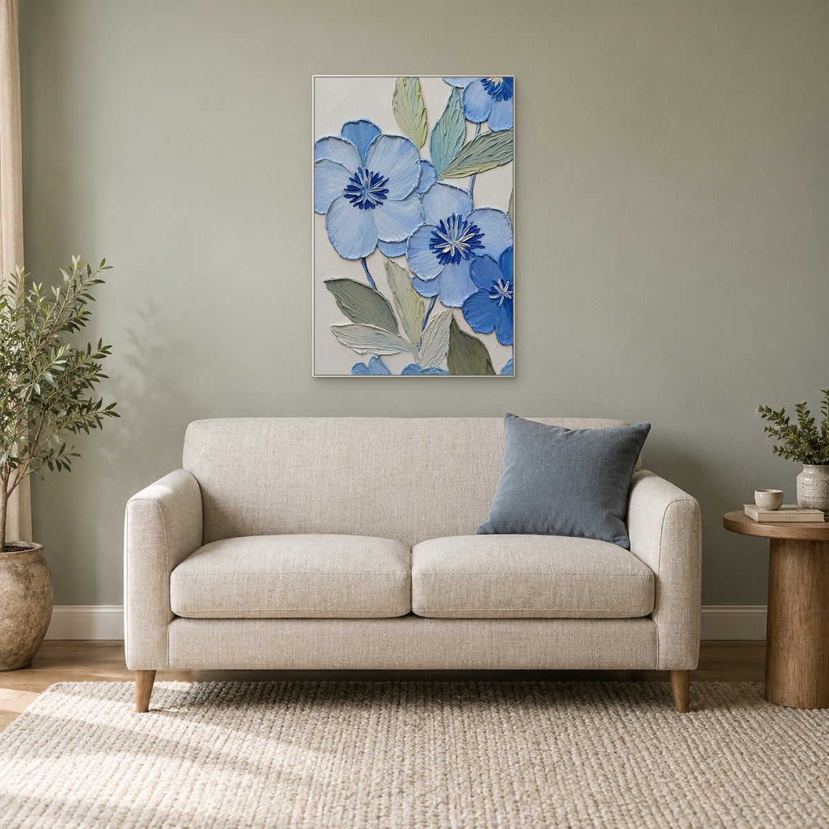 White-framed blue floral painting above a cream loveseat beside a leafy plant in a reading corner