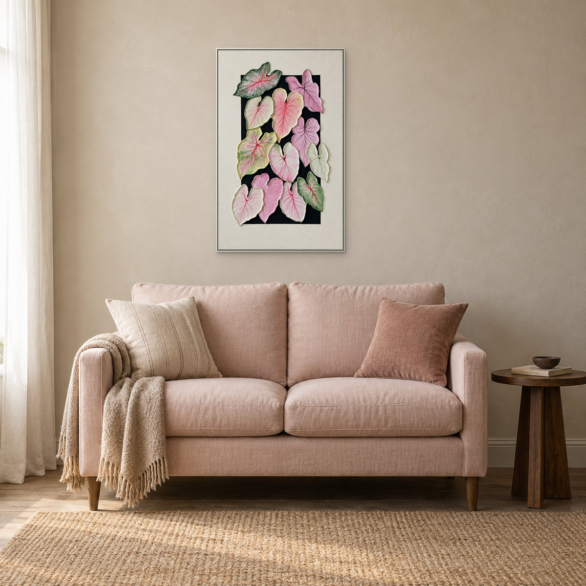Feuilles de caladium dans un cadre flottant blanc, centrées au-dessus d’un petit canapé rose poudré près d’une table en bois foncé