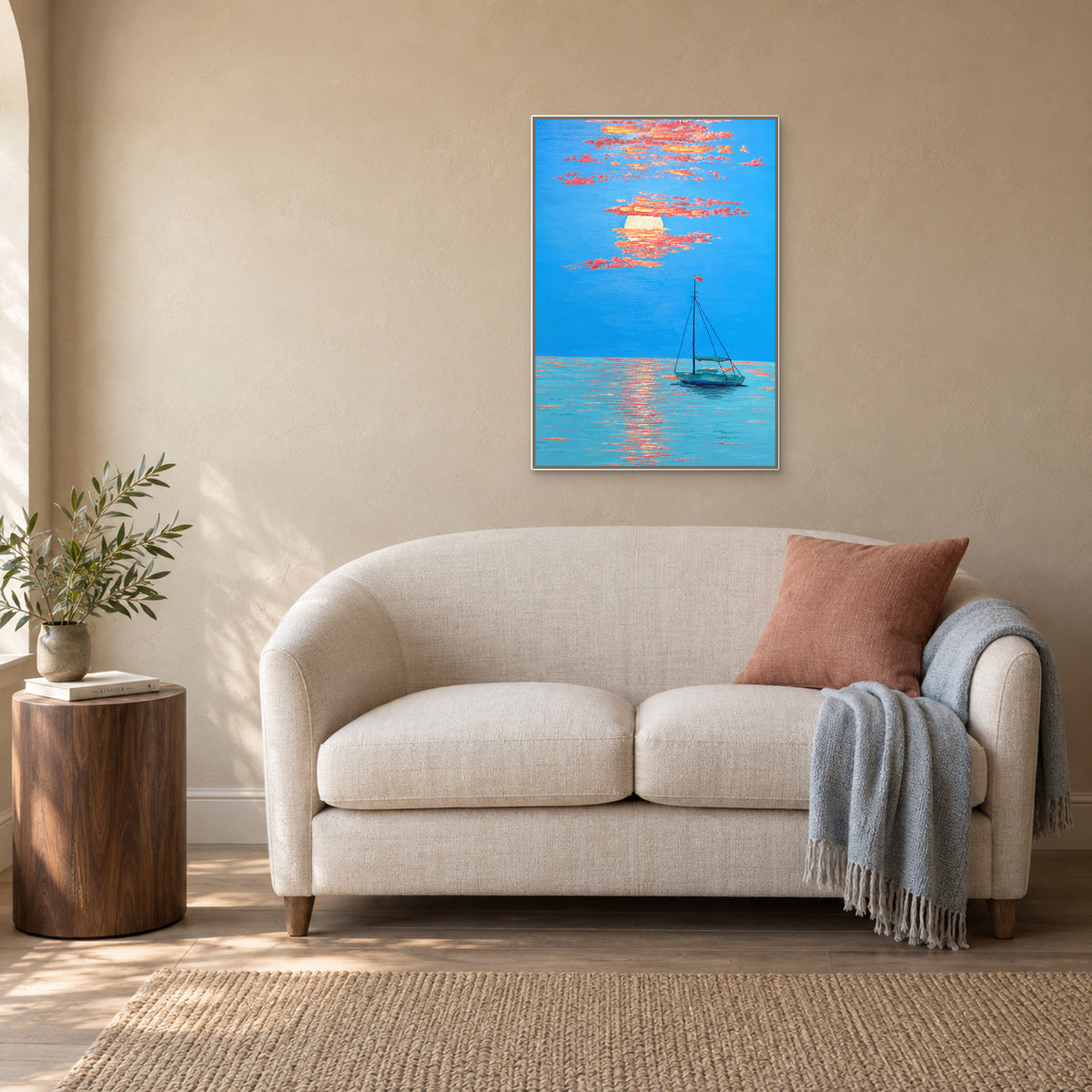 Paysage marin vertical au couchant, cadre flottant blanc, au-dessus d’un petit canapé crème avec coussin corail et plaid bleu pâle.