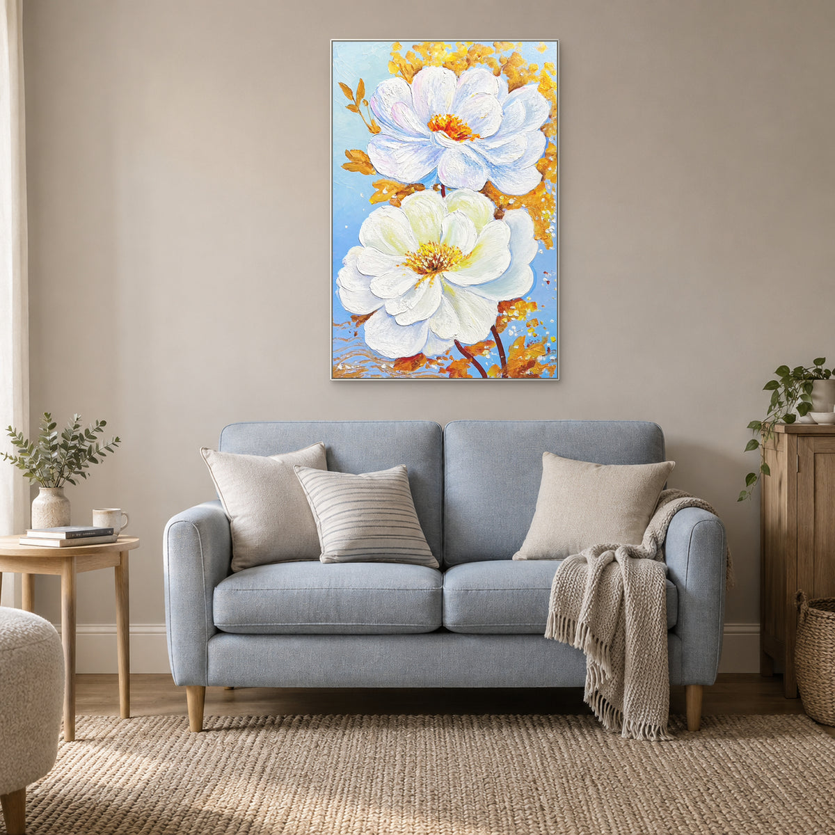 Two white blossoms in a white floating frame above a blue reading sofa with cream cushions.