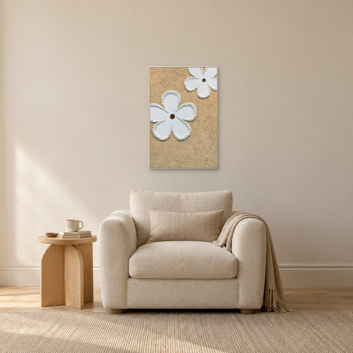 Two white flowers on beige in a white frame above a cream armchair, beside a small oak-toned table