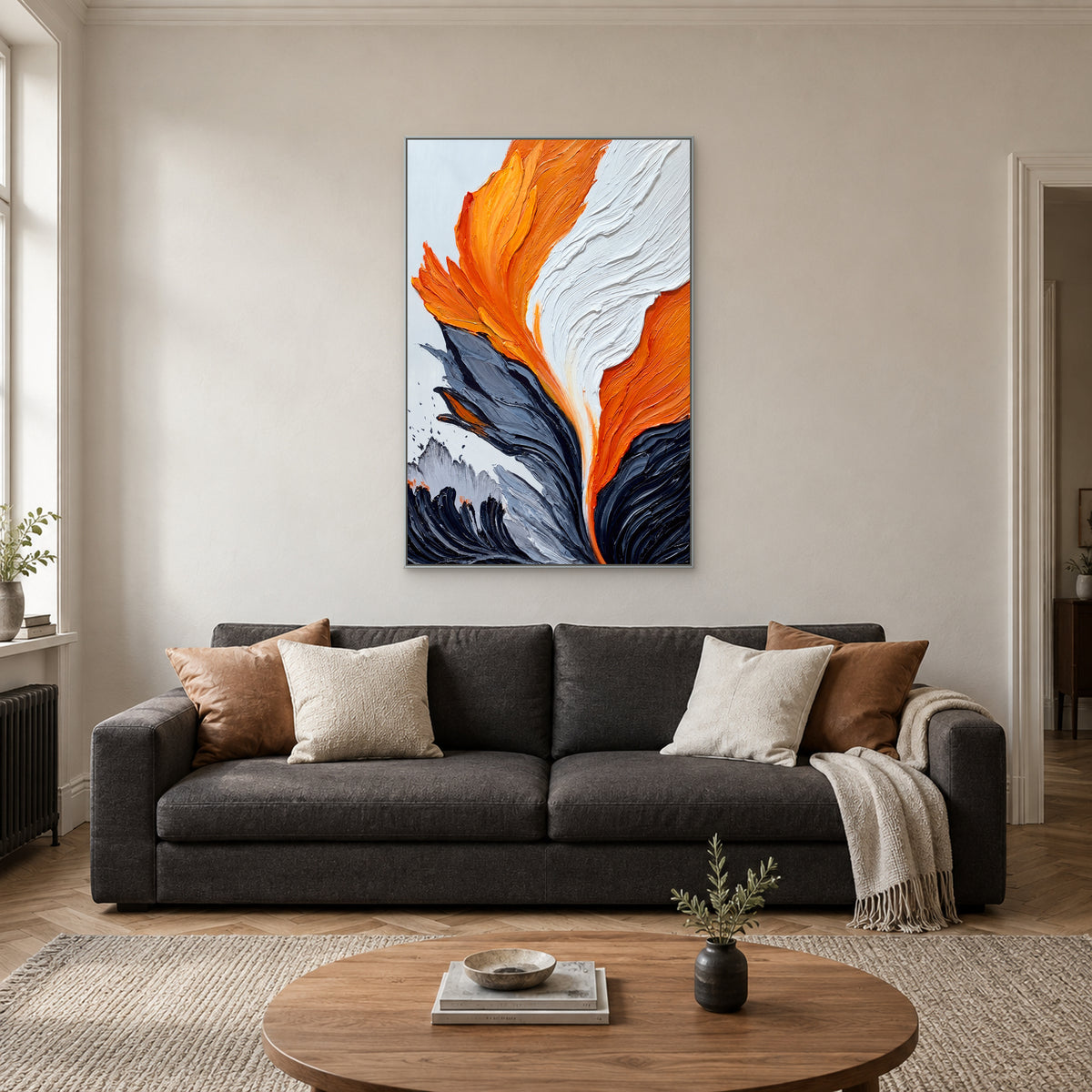 Tableau vertical orange, blanc et gris dans un cadre argenté, centré au-dessus d’un canapé anthracite