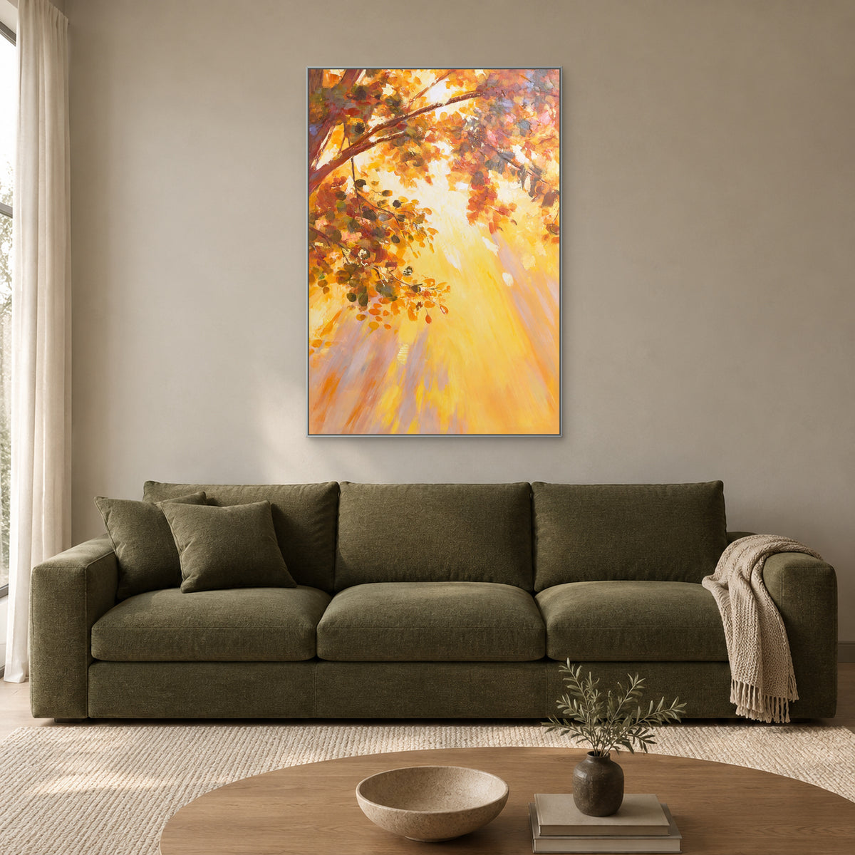 Warm autumn tree artwork in a slim silver frame above an olive sofa in a sunlit living room.