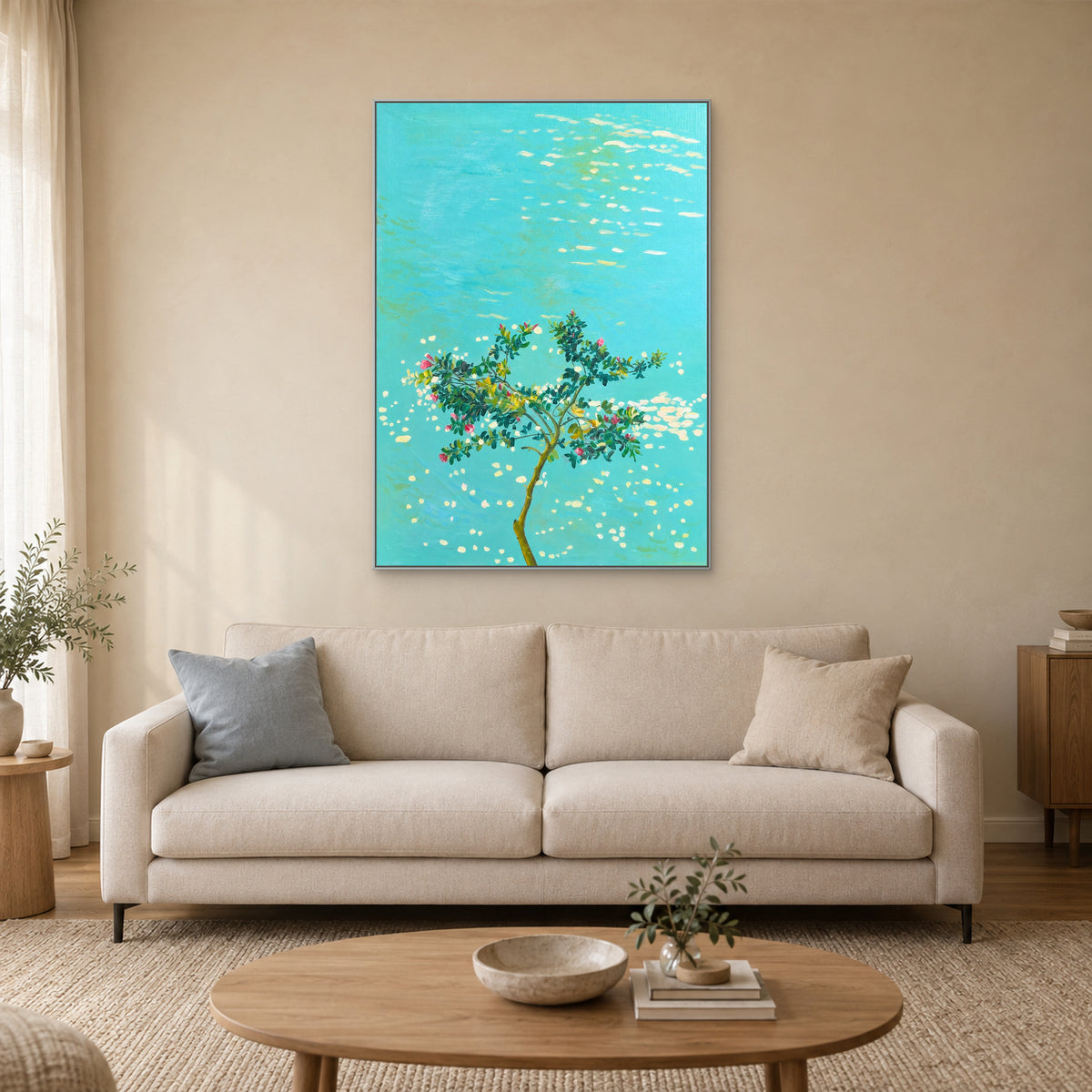 Tableau végétal turquoise dans un cadre argenté centré au-dessus d’un canapé crème sur un mur sable clair