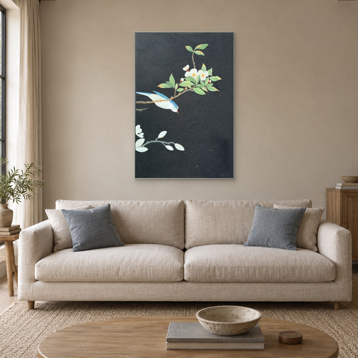 Charcoal-ground bird painting in a silver-tone frame above a pale sofa with blue-grey cushions