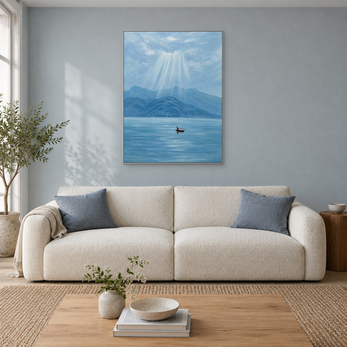 Blue lake and mountain painting in a silver-toned frame centred over a curved cream sofa against a muted blue wall