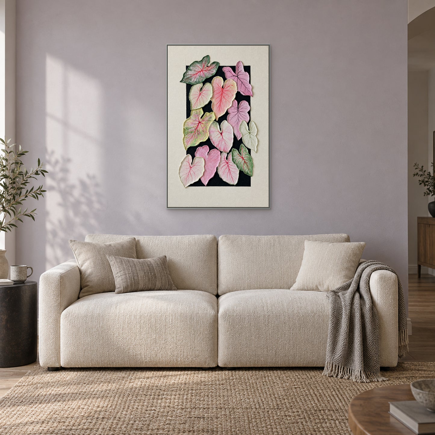 Composition texturée de feuilles de caladium dans un cadre flottant argenté, au-dessus d’un canapé crème contre un mur gris lilas pâle