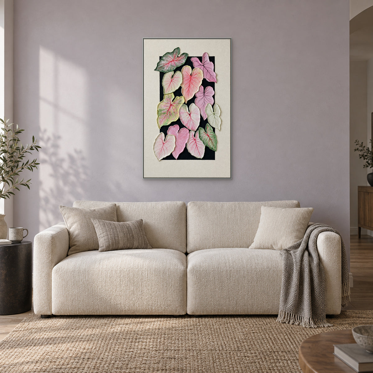 Composition texturée de feuilles de caladium dans un cadre flottant argenté, au-dessus d’un canapé crème contre un mur gris lilas pâle