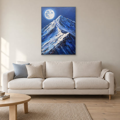 Tableau de pleine lune et de montagne encadré d’argenté, au-dessus d’un canapé crème aux coussins bleus et neutres