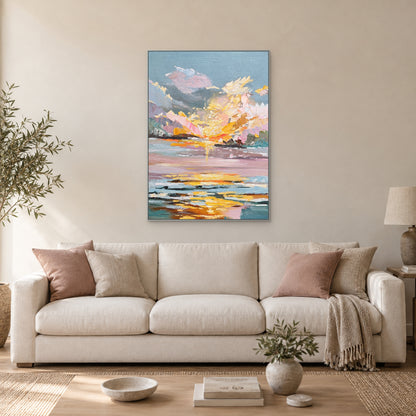 Pink and gold sunset landscape in a silver-tone frame above a cream sofa