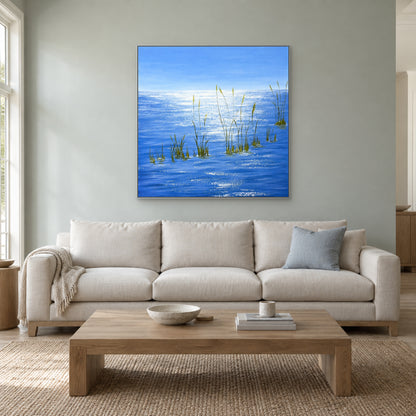 Tableau carré d’eau bleue dans un cadre argenté au-dessus d’un canapé crème, sur un mur gris-vert clair