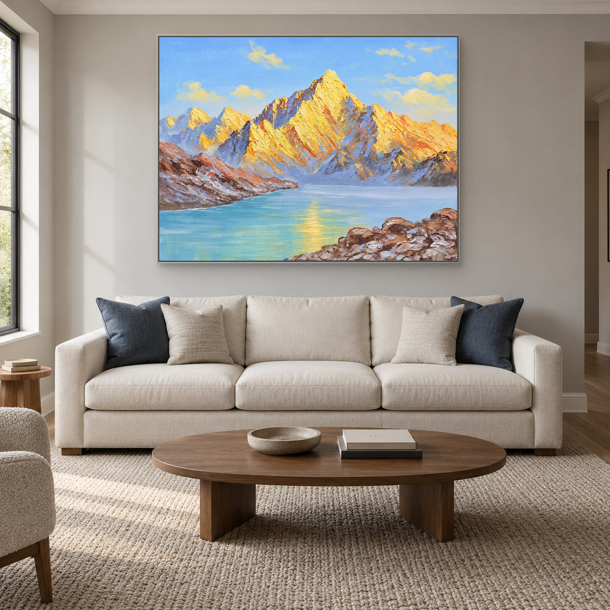 Tableau horizontal de montagnes dorées dans un cadre argenté, au-dessus d'un canapé crème aux coussins bleus