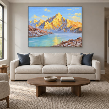Tableau horizontal de montagnes dorées dans un cadre argenté, au-dessus d'un canapé crème aux coussins bleus